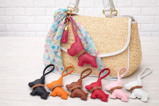 6 different colored Pocket Puppy Leather Bag Charms  with collar in a row in front of a straw bag.