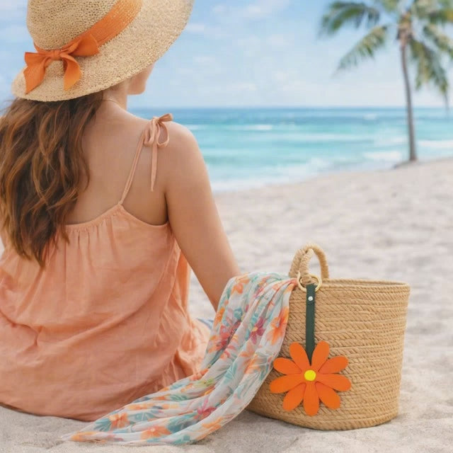 Video of Woman on Beach with Coral Petal Pop Bag Charm on a straw bag with scarf. 