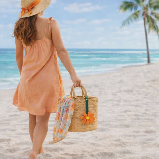 Video of Woman walking on Beach with Coral Petal Pop Bag Charm on a straw bag with scarf. 