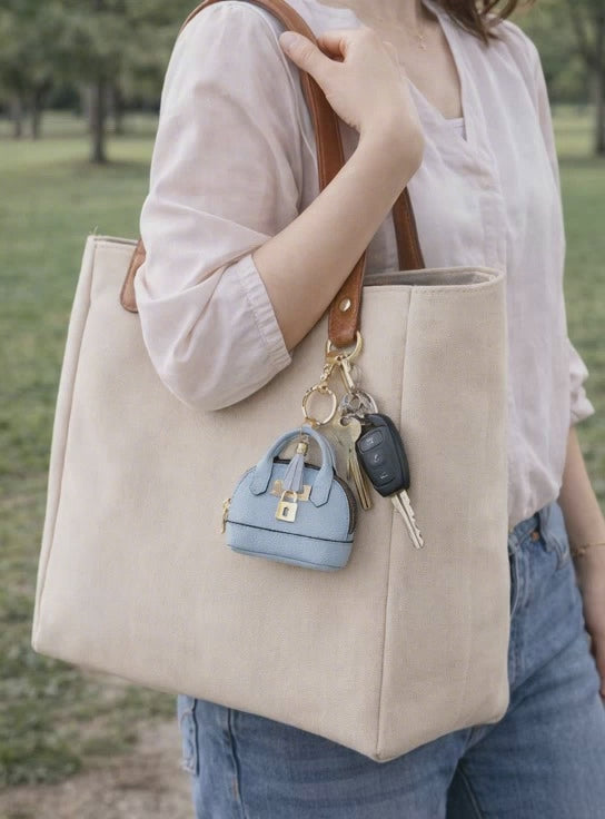 Video of women holding tan tote bag with light blue petite leather mini purse bag charm with keys attached.