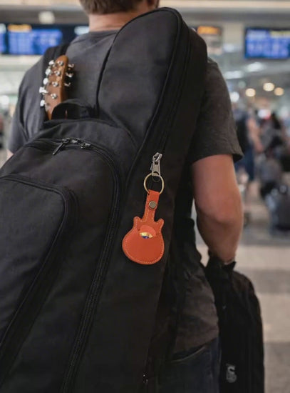 Video of Handmade orange guitar-shaped leather keychain with a secure pick pocket and brass-tone ring connected to black guitar case. 